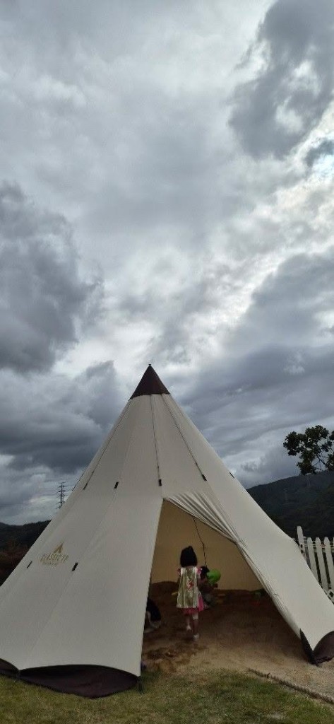 Child standing inside a cream teepee tent outdoors