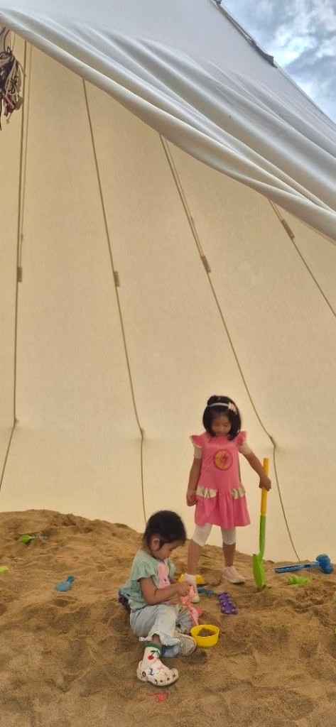 Two children playing in a sandpit inside a tent