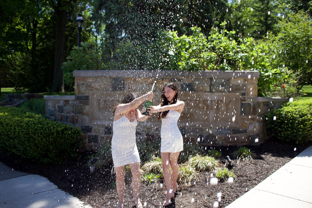 Friends spraying champagne beside a campus stone sign