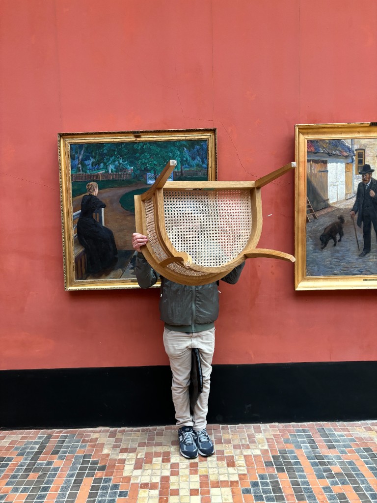 Holding a cane-seat wooden chair in a gallery